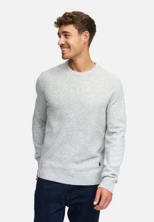 Grå stickad tröja med rund halsringning, ribbad fåll och ribbade manschetter. Mjuk textur, med en liten brun etikettdekoration på sidan.