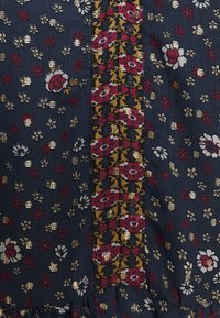 Tissu sombre avec de petits motifs floraux rouges, gris et dorés, présentant une bande verticale de grandes fleurs rouges avec des accents dorés.