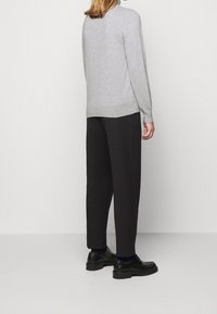 Maglione grigio lavorato a maglia, vestibilità ampia, maniche lunghe. Pantaloni neri a gamba larga e scarpe nere. Design minimalista, texture liscia.