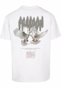 Hvid bomulds T-shirt med et grafisk motiv af to duer med udfoldede vinger, omgivet af en cirkulær kontur, og ordet "FREEDOM" i fed grå tekst.
