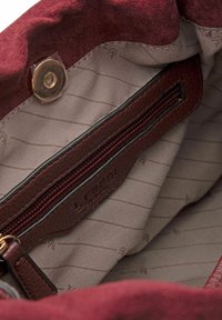 Interno della borsa in suede bordeaux con fodera in tessuto beige. Presenta una tasca con zip marrone e un marchio stampato sulla tasca.
