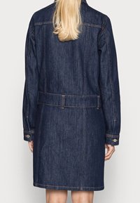 Denim coat featuring a dark blue color, long sleeves, belted waist, and buttoned cuffs, with visible stitching detail. Back view displayed.