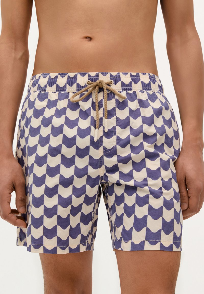 Pantaloni de baie dintr-un material ușor, cu un model de valuri în crem și bleumarin, având o talie elastică și detalii cu șnur bej.