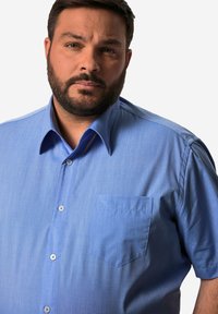 Camisa de manga corta de color azul claro hecha de tejido texturizado; cuenta con un cierre frontal de botones y un bolsillo en el pecho.
