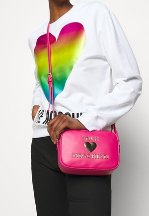 Růžová kožená kabelka přes rameno se zlatými písmeny "LOVE MOSCHINO" a motivem srdce. Hladká struktura a obdélníkový tvar. Nastavitelný popruh.