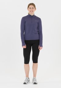 Pitkähiha, vetoketjullinen violetti urheiluyläosa yhdistettynä mustiin capri-leggingseihin ja harmaisiin lenkkareihin. Silkkinen pinta, tiukka malli, minimaalinen brändäys.