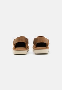 Bruna sandaler med dubbla kardborreband, en dämpad fotbädd och en ljusgummisula. Utformade för avslappnad användning och komfort.