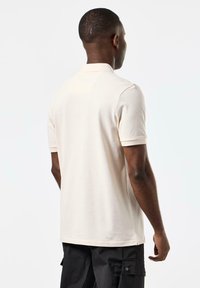 Beige polo skjorte med korte ermer, laget av et mykt materiale. Enkel design med klassisk krage og sidesplitter i nederkant.