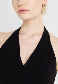 Black halter neck dress featuring a deep V neckline, smooth texture, and minimal stitching details. Elegant and streamlined design.