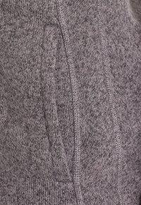 Tejido de punto gris Heather con un primer plano de una costura vertical y una abertura de bolsillo lateral parcialmente visible.