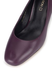 Lila Lederpumpe mit abgerundetem Zehenbereich und glatter Textur, versehen mit einem schwarzen Innenfutter und dezenten Markenakzenten.