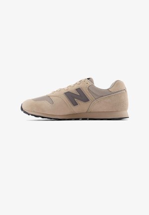 Beige New Balance sneaker met suède en mesh panelen, zwart logo aan de zijkant en zwarte rubberen zool, zijaanzicht op witte achtergrond.