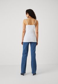Hvit ermeløs topp med tynne stropper, kombinert med blå denim bellbottom bukser med prikkete mønster og en lett glans.