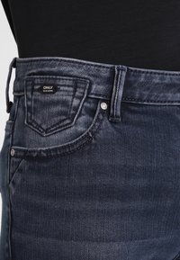 Blå denimjeans med klassisk skärning, framfickor och varumärkesetikett "ONLY" på midjan. Har en slät textur och mörk tvätt.