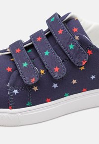 Sneaker din pânză bleumarin cu un model de stele multicolore, talpă din cauciuc alb și trei curele cu arici pentru închidere.