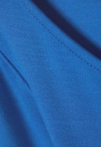 Nahaufnahme von leuchtend blauer Strickware, die Textur und Nähdetails mit sanften Falten und Schatten zeigt.