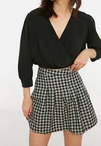 Blusa nera avvolgente con maniche a tre quarti abbinata a una gonna plissettata a quadri bianchi e neri con vita alta.