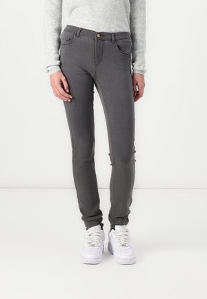 Jeans skinny grises con una textura suave, bolsillos frontales y cierre de botón, combinados con zapatillas blancas, usados sobre un suéter ligero.