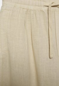 Pantalon en lin beige clair avec une taille élastique, une poche latérale et un cordon de serrage sur le côté droit.
