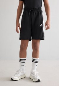 Melni sporta šorti ar elastīgu jostu, ar baltām sānu svītrām un mazu baltu logo. Saskaņoti ar baltiem, svītrainiem zeķēm un sporta apaviem.