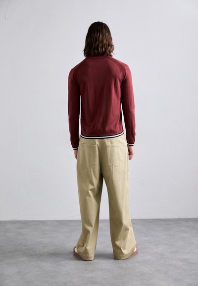 Maglietta a maniche lunghe color marrone scuro con colletto a contrasto bianco e nero, abbinata a pantaloni beige a gamba larga. Tessuto liscio, design casual.