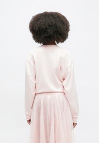 Απαλό ροζ φούτερ με μαλακή υφή και άνετη γραμμή, συνδυασμένο με διαφανή, στρωματοποιημένη ροζ τούλινη φούστα. Βλέπουμε από την πίσω πλευρά.