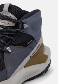 Buty trekkingowe z cholewką o zróżnicowanej fakturze w kolorach granatowym, szarym i beżowym. Zauważalna metka Gore-Tex, trwałe sznurowanie i strukturzona podeszwa gumowa.