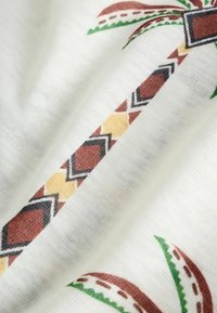 Tissu blanc avec un motif de palmier présentant un tronc marron, jaune et noir à motif et des frondes vertes et brunes.