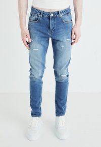 Ljusblå denimjeans med slim fit, som har slitna detaljer och knappstängning. Kombineras med vita sneakers.