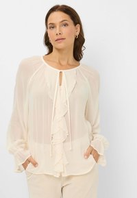 Cream blouse with ruffled front, round neckline, and drawstring closure. Long sleeves with gathered cuffs. Lightweight, sheer fabric.