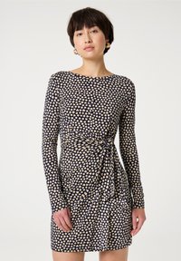 Navyblaues Kleid mit langen Ärmeln, das ein cremefarbenes Herzmuster aufweist, eine taillierte Passform hat und ein Seitennudel-Detail an der Taille besitzt. Glatte Textur.