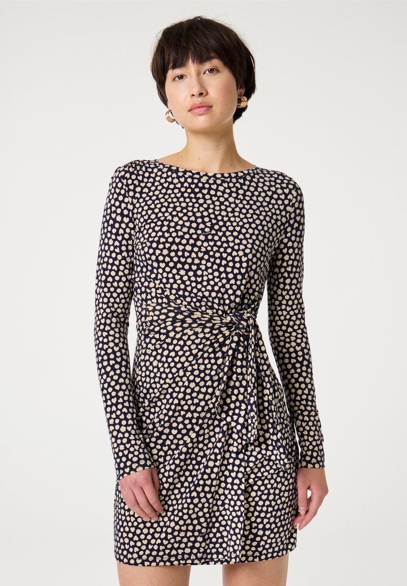 Navyblaues Kleid mit langen Ärmeln, das ein cremefarbenes Herzmuster aufweist, eine taillierte Passform hat und ein Seitennudel-Detail an der Taille besitzt. Glatte Textur.