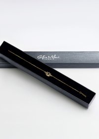 Bracciale d'oro con charm a forma di fiore di loto, esposto in una scatola nera con interno in satin. La catena presenta una lunghezza regolabile.