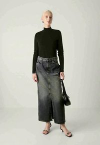 Top preto de manga longa combinado com uma saia maxi de ganga escura, com uma fenda frontal e desbotamento suave. Acessório incluído é uma pequena bolsa preta.