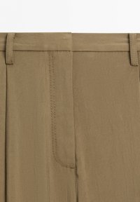 Close-up of tan pants waistband showing belt loops and front fly stitching details.