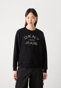 Svart hettegenser med rund hals, med en glitrende "DKNY Jeans 1989" trykk. Myk stoff, avslappet passform og ribbestrikkede mansjetter.