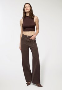 Brązowy, krótki top na ramiączkach w połączeniu z brązowymi, szerokimi spodniami o wysokim stanie. Outfit cechuje się prostym designem, bez wzorów czy ozdób.