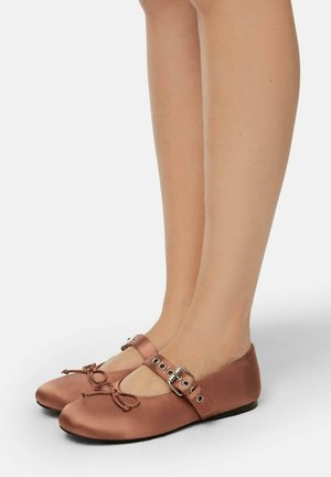 Ballet flats in light brown satin with a round toe, bow detail at the front, and a wide strap featuring a metallic buckle and eyelets.