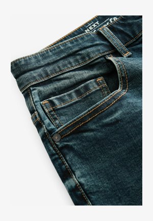 Jeans in denim blu scuro con una finitura sbiadita, caratterizzati da cuciture arancioni, una tasca frontale e un dettaglio con bottone metallico in vita.