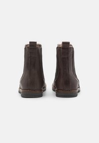 Botines de cuero marrón con paneles laterales elásticos, parte trasera texturizada y suelas planas de goma. Presentan costuras en el borde y lengüetas para facilitar su puesta.