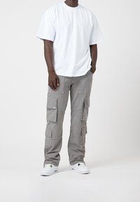 T-shirt en coton blanc à manches courtes, assorti à un pantalon cargo gris clair avec plusieurs poches et un tissu résistant. Baskets blanches avec des accents.