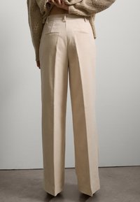 Cremfarbene weite Cordhosen mit glatter Textur, Frontfalten und doppelten Gesäßtaschen. Taillierter Schnitt mit strukturiertem Design.