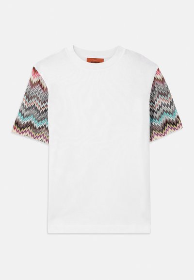 Valge lühikeste varrukatega T-särk, millel on mustrilised kudumivarrukad, mis sisaldavad mitmevärvilisi zikk-zakk kujundusi roosa, sinise, halli ja musta aktsendiga.