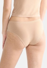 Culotte en mélange de coton beige avec une texture lisse, dotée d'une large ceinture élastique et d'un design couvrant, vue de l'arrière.