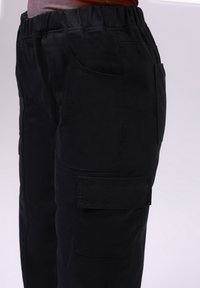 Pantalon cargo noir avec une ceinture élastique, des poches latérales et une texture lisse ; présente une coupe décontractée et un design de style utilitaire.