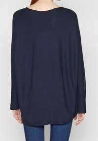 Pull marin surdimensionné, tissu tricoté, large encolure bateau, manches longues, ourlet arrondi, texture douce, coupe décontractée, surpiqûres détaillées le long des bords.