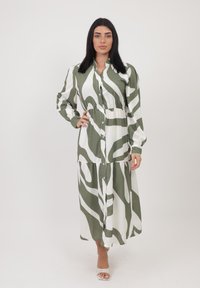 Lungo vestito con bottoni in tessuto leggero, caratterizzato da un motivo astratto verde e bianco. Ha maniche lunghe e un design a gonna a strati.