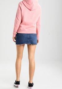 Sudadera rosa con capucha, combinada con una mini falda de mezclilla azul con bordes deshilachados. Usada con zapatillas negras.