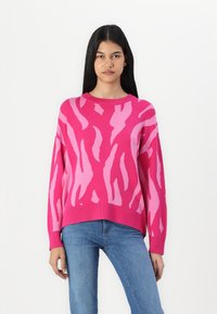 Rosa tröja med abstrakta ljusrosa mönster, rund halsringning, långa ärmar, ribbade ärmslut och nederkant, ihopparad med blå jeans.
