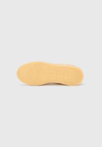 Ελαφρώς καφέ σόλα αθλητικού παπουτσιού με παχύ, υφασμάτινο λαστιχένιο υλικό. Διαθέτει κυματιστό σχέδιο πέλματος και λεπτομέρεια με λογότυπο στο κέντρο.